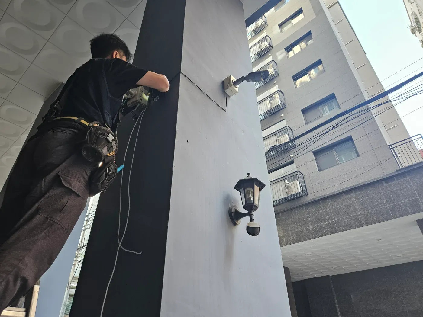 기사가 건물 기둥에서 CCTV 배선 작업을 하는 모습